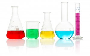 gelas laboratorium diisi cairan warna-warni ing latar mburi putih