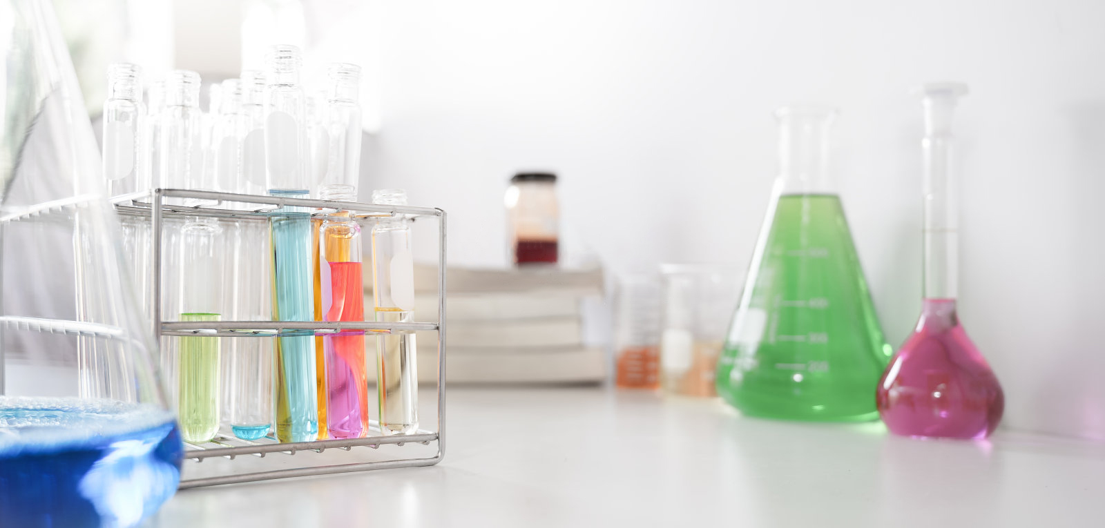 صورة لأدوات زجاجية مختبرية تحتوي على سوائل ملونة أثناء تجميعها على طاولة بيضاء معزولة على خلفية بيضاء.